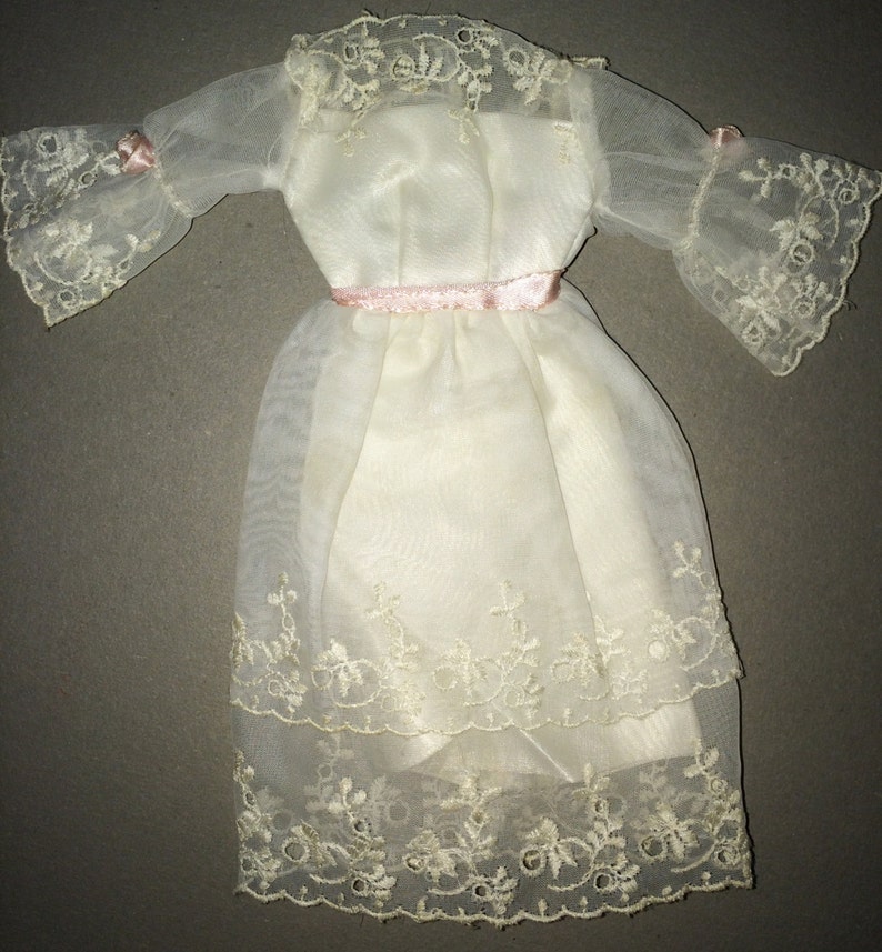 Puede incluir: Un vestido blanco de gasa con delicados detalles de encaje y una cinta de raso rosa alrededor de la cintura.