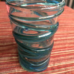 May include: A clear glass drinking glass with a blue and green swirl design.