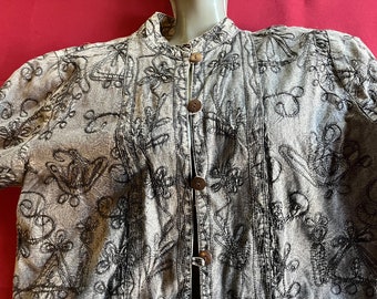 May include: A gray cotton jacket with a black embroidered floral pattern. The jacket has a mandarin collar and a button closure.