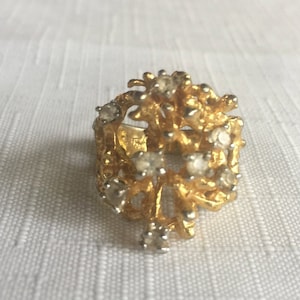 Puede incluir: Un anillo de oro con un diseño delicado e intrincado que presenta un grupo de diamantes de imitación transparentes. El anillo tiene un aspecto texturizado y orgánico, que recuerda a una flor o rama estilizada.