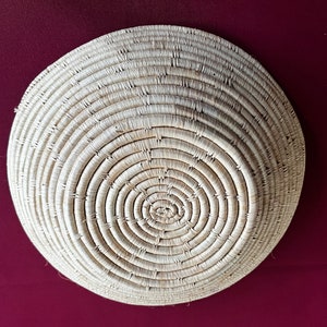 Könnte beinhalten: Ein großer, runder, geflochtener Korb aus natürlichen Materialien. Der Korb ist hellbraun und hat ein kreisförmiges Muster aus geflochtenen Strängen.