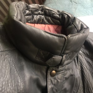 Pu&ograve; includere: Una giacca di pelle grigio scuro con un colletto alto e una chiusura con bottoni. Il colletto &egrave; foderato con un tessuto bordeaux.