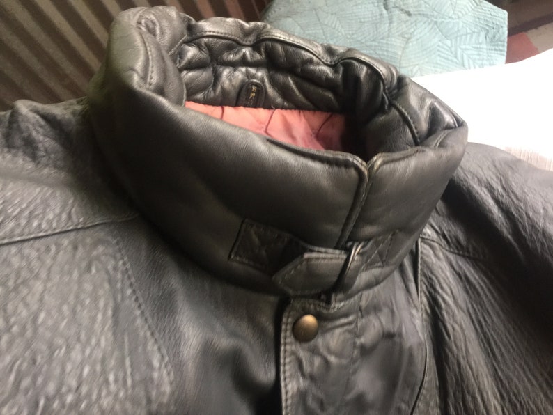 Pu&ograve; includere: Una giacca di pelle grigio scuro con un colletto alto e una chiusura con bottoni. Il colletto &egrave; foderato con un tessuto bordeaux.
