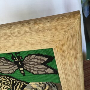 May include: A framed needlepoint picture with a green background and a butterfly design. The frame is made of wood and has a light brown finish.