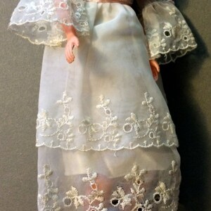 Puede incluir: Un vestido blanco de encaje con una cinta rosa en la cintura. El vestido es de tela transparente y tiene bordados delicados.