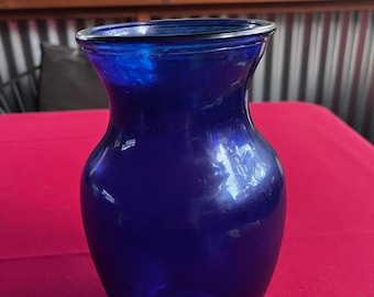 May include: A cobalt blue glass vase with a rounded body and a flared opening. The vase is sitting on a red surface.
