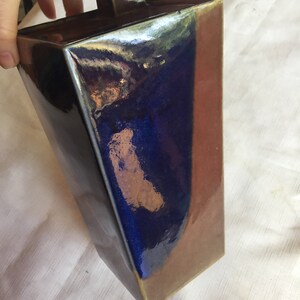 Op de afbeelding: Een rechthoekige keramische vaas met een donkerblauwe en bruine glazuur. De vaas heeft een vierkante bovenkant en een licht afgeronde bodem.