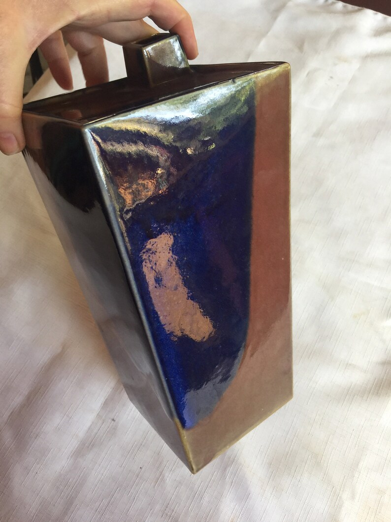 Op de afbeelding: Een rechthoekige keramische vaas met een donkerblauwe en bruine glazuur. De vaas heeft een vierkante bovenkant en een licht afgeronde bodem.