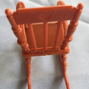 K&ouml;nnte beinhalten: Ein Miniatur-Schaukelstuhl aus braunem Kunststoff. Der Stuhl hat ein einfaches Design mit einer geschwungenen R&uuml;ckenlehne und vier Beinen.