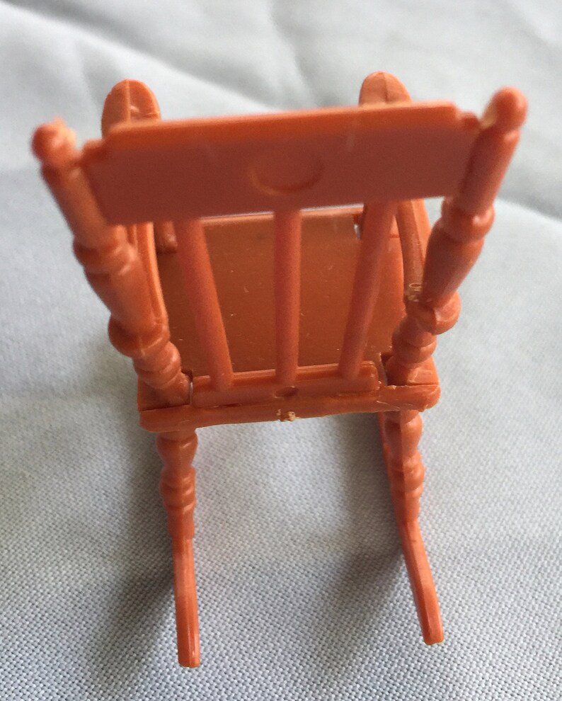 K&ouml;nnte beinhalten: Ein Miniatur-Schaukelstuhl aus braunem Kunststoff. Der Stuhl hat ein einfaches Design mit einer geschwungenen R&uuml;ckenlehne und vier Beinen.