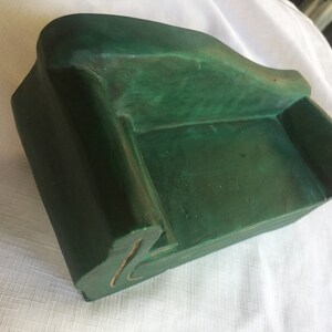 May include: A small, green, wooden sofa shaped like a couch. The sofa is made of wood and painted a deep green color.
