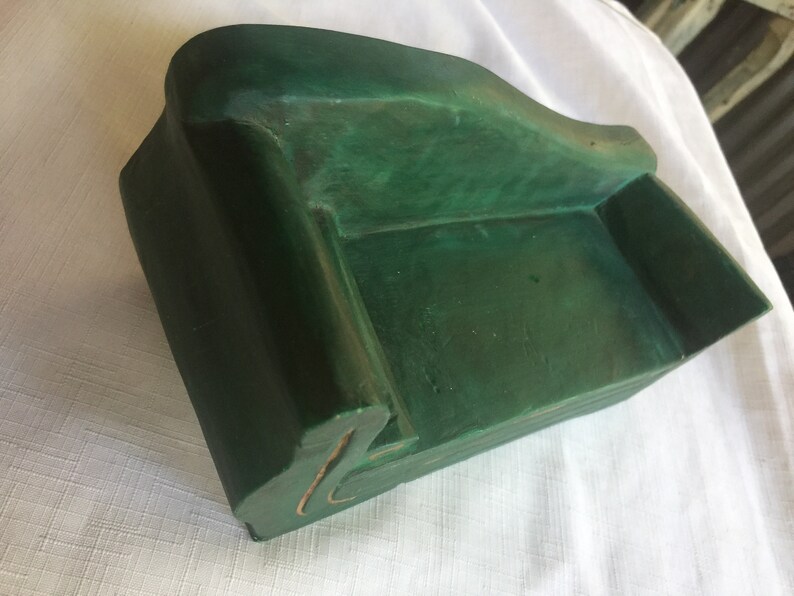May include: A small, green, wooden sofa shaped like a couch. The sofa is made of wood and painted a deep green color.