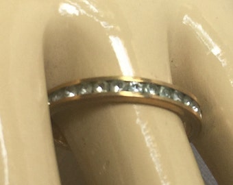 May include: A gold band ring with a row of small clear stones.