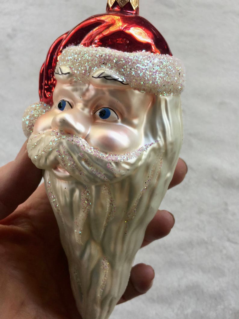 以下が含まれることがあります： サンタクロースの頭の形をしたクリスマスオーナメント。白いグリッターのトリムが付いた赤い帽子、青い目、グリッター付きの長い白いひげが特徴です。お祝いのホリデーデコレーション。