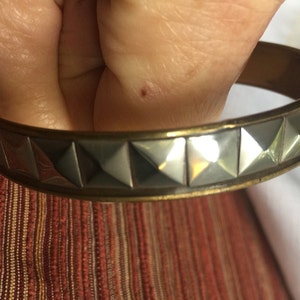 Può includere: Un braccialetto rigido in argento e oro con una fila di borchie a forma di piramide.