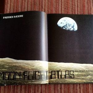 May include: An open book titled "Moon Flight Atlas" by Patrick Moore. The cover shows a dark background with an image of the Earth and a depiction of the moon's surface. Published by Rand McNally & Company.