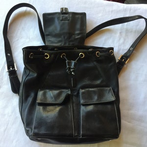 May include: Black leather backpack with a drawstring closure and two front pockets. The backpack has gold-toned hardware and adjustable straps.