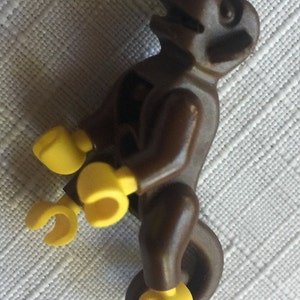 May include: A brown plastic toy monkey riding a yellow plastic unicycle. The monkey has a brown head with a black face and yellow hands and feet.