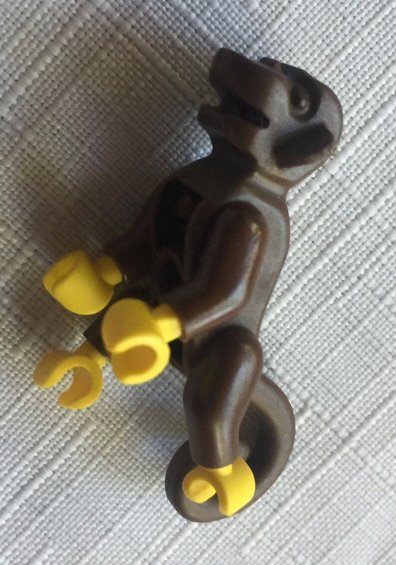 May include: A brown plastic toy monkey riding a yellow plastic unicycle. The monkey has a brown head with a black face and yellow hands and feet.