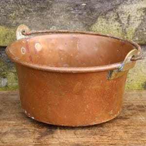 May include: A vintage copper pot with a brass handle. The pot has a worn, rustic look and is perfect for adding a touch of farmhouse charm to your kitchen.