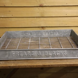 May include: A rectangular galvanised metal tray with a wire grid base. The tray has the embossed text "FREARS & BLACKS" on the front and "Sᴚ∀Ǝᖵ & S⅄Ɔ∀ꓘS" on the back. The tray is on a wooden surface.