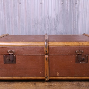 May include: A rectangular brown storage trunk featuring a textured surface, light wood trim along the edges, and vertical wooden slats. The trunk includes dark metal corner reinforcements, two front metal latches, and a central metal locking mechanism.