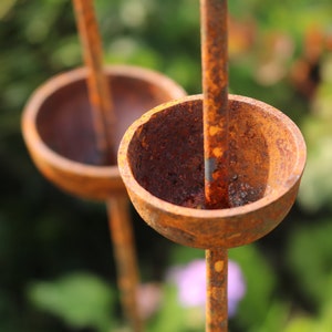May include: A close-up of a rusty metal garden sculpture with three round, bowl-shaped elements. The sculpture is made of metal rods and has a rustic, weathered look.