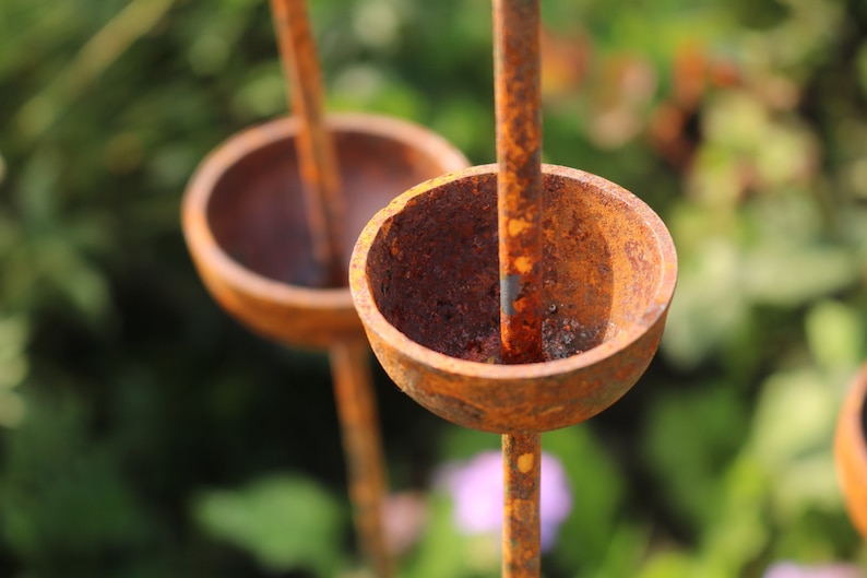 May include: A close-up of a rusty metal garden sculpture with three round, bowl-shaped elements. The sculpture is made of metal rods and has a rustic, weathered look.