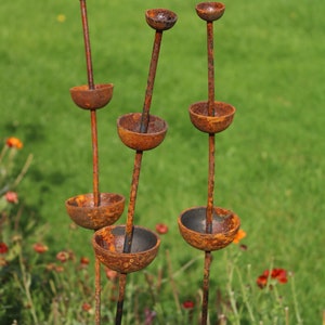May include: Four rusty metal sculptures with rounded bowls stacked on top of each other. The sculptures are standing upright in a grassy field.