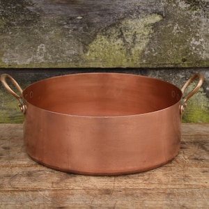 May include: A copper pot with two handles. The pot is shiny and has a rounded bottom.
