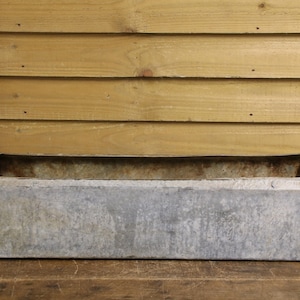 May include: A rectangular, galvanised metal trough with a weathered, silver-grey finish. The container features straight sides, a flat base, and visible signs of oxidation and patina across its exterior surface, presenting a utilitarian design.