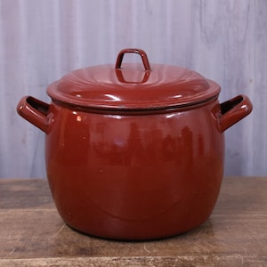 May include: A deep, round, dark red enamelled metal stockpot with a matching lid. The pot features two side handles and a small handle on the centre of the lid. The exterior has a smooth, glossy finish with a consistent deep red colour throughout.