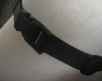 May include: A black adjustable belt with a plastic buckle. The belt is made of a woven material and has a smooth finish.