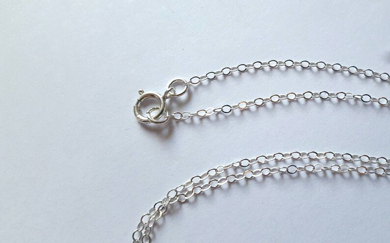 May include: A silver chain necklace with a lobster clasp closure. The chain is made of small, round links.