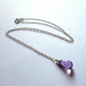 May include: A delicate silver chain necklace with a single, teardrop-shaped amethyst pendant.