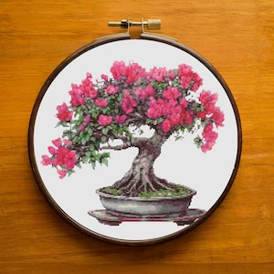 May include: A pink and green bonsai tree with flowers in a brown pot. The tree is in a round wooden frame.