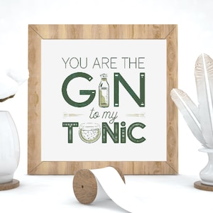 Könnte beinhalten: Gerahmter Druck mit dem Text "YOU ARE THE GIN to my TONIC" in grünen Buchstaben. Das Kunstwerk zeigt Illustrationen einer Gin-Flasche und eines Cocktailglases. Der Rahmen ist aus hellem Holz.