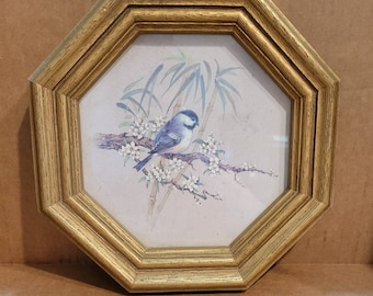 May include: An octagonal framed print featuring a blue and white bird perched on a flowering branch. The artwork includes bamboo stalks in the background and is set within a gold-toned wooden frame. A decorative piece for home decor.