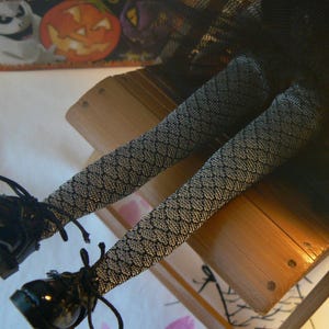Peut inclure: Chaussures vernies noires à lacets et bas à motifs. Les bas ont un motif en losange. Les jambes reposent sur une surface en bois. Une décoration sur le thème d'Halloween est en arrière-plan.