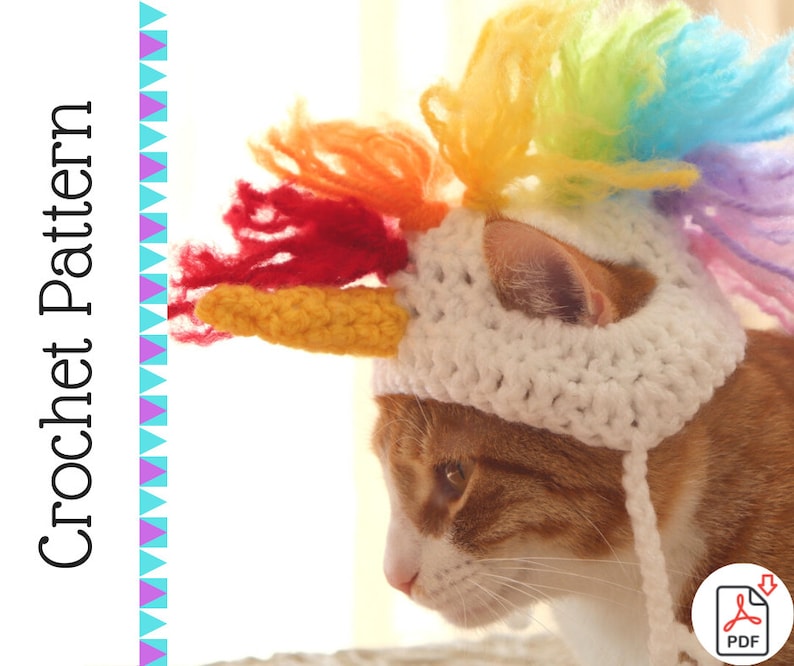 May include: A white crocheted cat hat with a rainbow mane and a yellow horn. The hat is on a cat with orange fur.