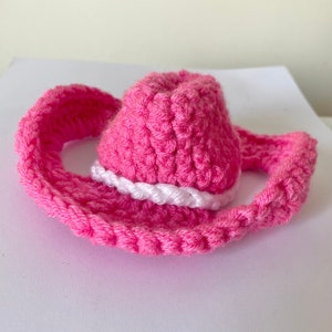 K&ouml;nnte beinhalten: Ein rosa geh&auml;kelter Cowboyhut mit einem wei&szlig;en geh&auml;kelten Band um die Krone.