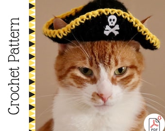 Könnte beinhalten: Eine rot-weiße Katze mit einem schwarzen gehäkelten Piratenhut mit einem weißen Totenkopf- und gekreuzten Knochen-Emblem. Der Hut hat eine gelbe Bordüre. Das Bild enthält den Text "Crochet Pattern".