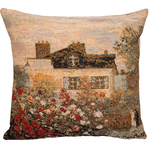 May include: A tapestry pillow featuring a beige house with a brown roof and red flowers in the foreground. The house has a cross on the window and a chimney. The background is a light blue sky.