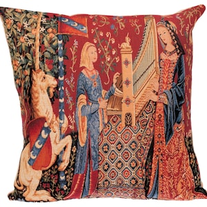 May include: A tapestry cushion featuring a unicorn, a woman playing a harp, and a woman in a blue dress. The tapestry is set against a red background with floral designs.
