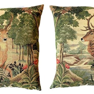 May include: Two decorative throw pillows with a tapestry design featuring a deer in a forest setting. The pillows are beige with green, brown, and red accents.