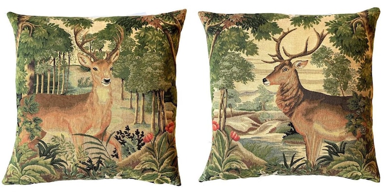 May include: Two decorative throw pillows with a tapestry design featuring a deer in a forest setting. The pillows are beige with green, brown, and red accents.