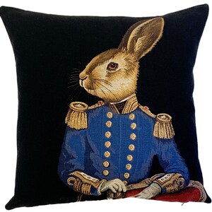 May include: A black throw pillow with a tapestry design of a rabbit wearing a blue military uniform with gold trim and buttons. The rabbit has brown fur and is looking to the left.