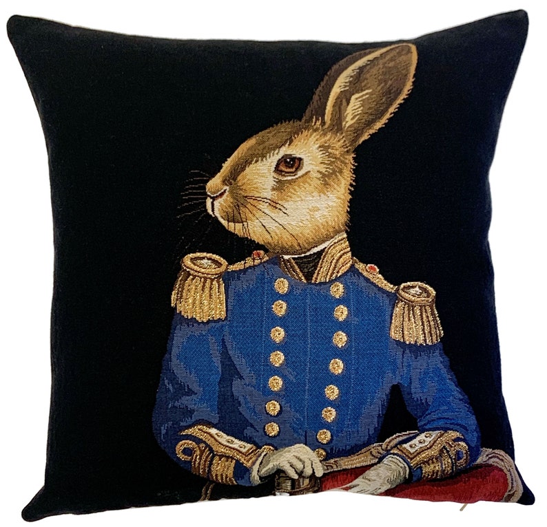 May include: A black throw pillow with a tapestry design of a rabbit wearing a blue military uniform with gold trim and buttons. The rabbit has brown fur and is looking to the left.