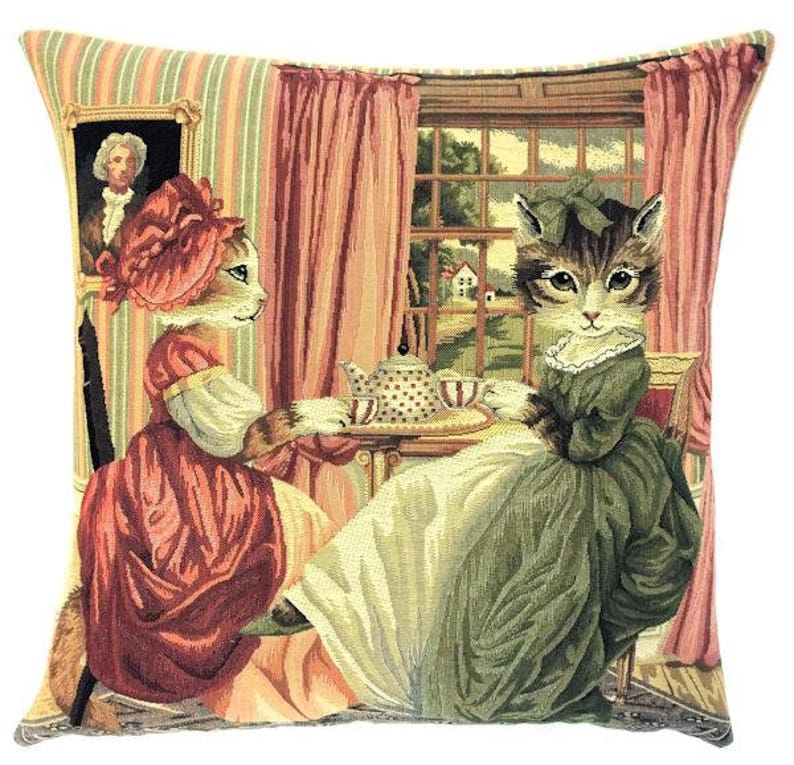 Op de afbeelding: Twee katten gekleed in vintage kleding drinken thee in een kamer met een raam en een gestreept behang. De kat links draagt een rode jurk en een roze muts. De kat rechts draagt een groene jurk en een groene muts. Ze zitten aan een tafel met een theepot en kopjes.