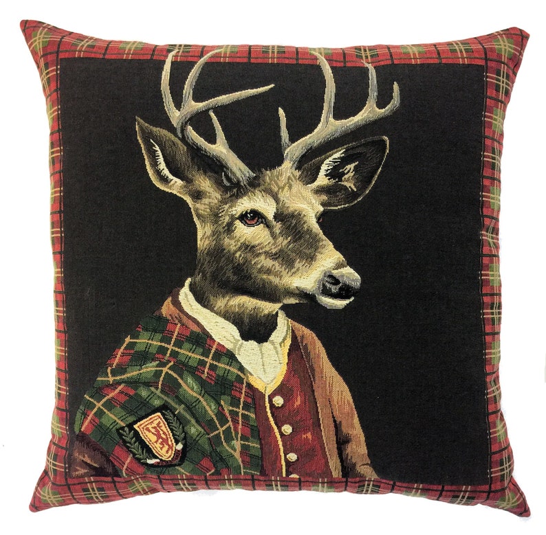 May include: A decorative cushion with a black background featuring a deer wearing a plaid kilt and a red waistcoat. The deer has large antlers and a serious expression. The cushion has a red and green tartan border.